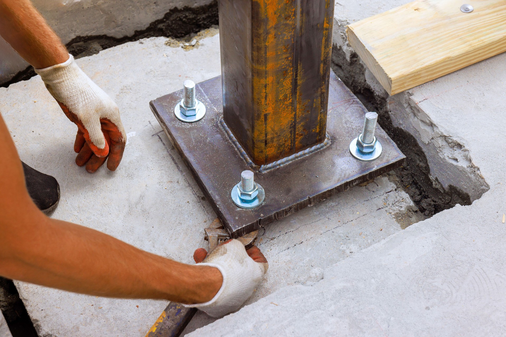 Construction worker installing steel support column on concrete foundation at building site in daylight